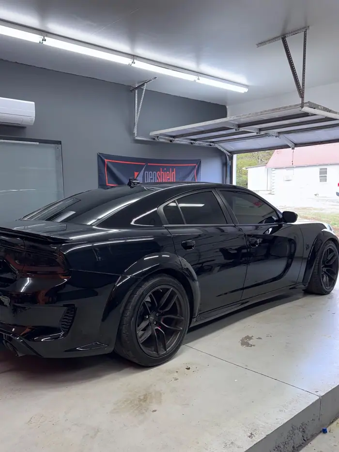 Gloss black Dodge Charger widebody in the Stealth Tint and PPF bay, Geoshield banner on the wall