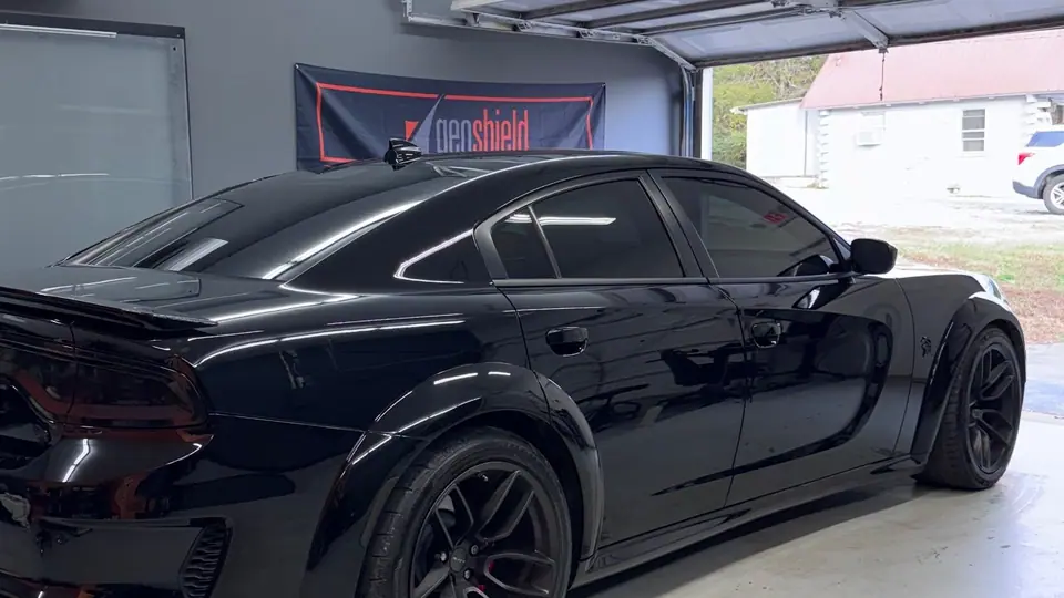Gloss black Dodge Charger widebody in the Stealth Tint and PPF bay with the garage door open