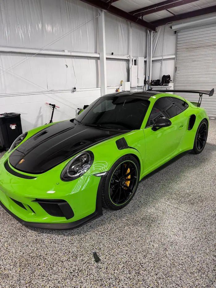 Lizard green Porsche 911 GT3 RS with a black hood and tinted glass inside a shop