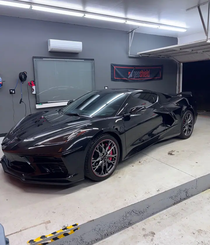 Black C8 Corvette with tinted glass parked in the Stealth Tint and PPF bay under LED light bars