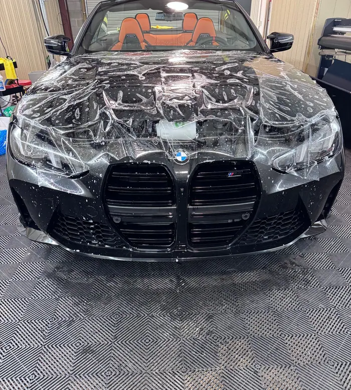 Clear paint protection film being laid wet over the hood and bumper of a black BMW M4