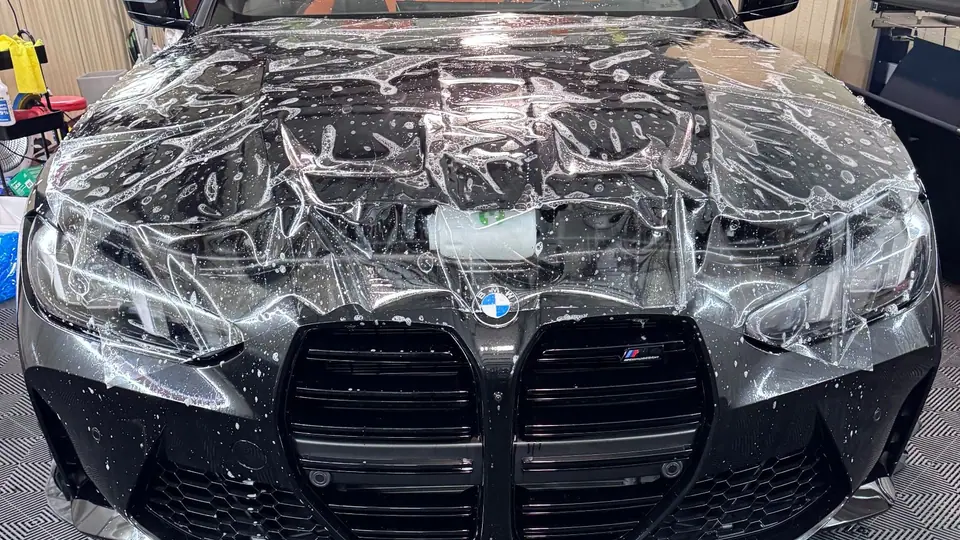 Clear paint protection film laid wet over the hood and headlights of a black BMW M4 during install