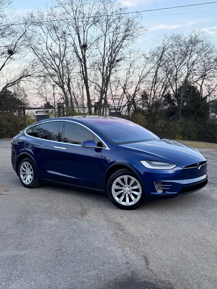 Blue Tesla Model X with tinted glass parked on asphalt at dusk