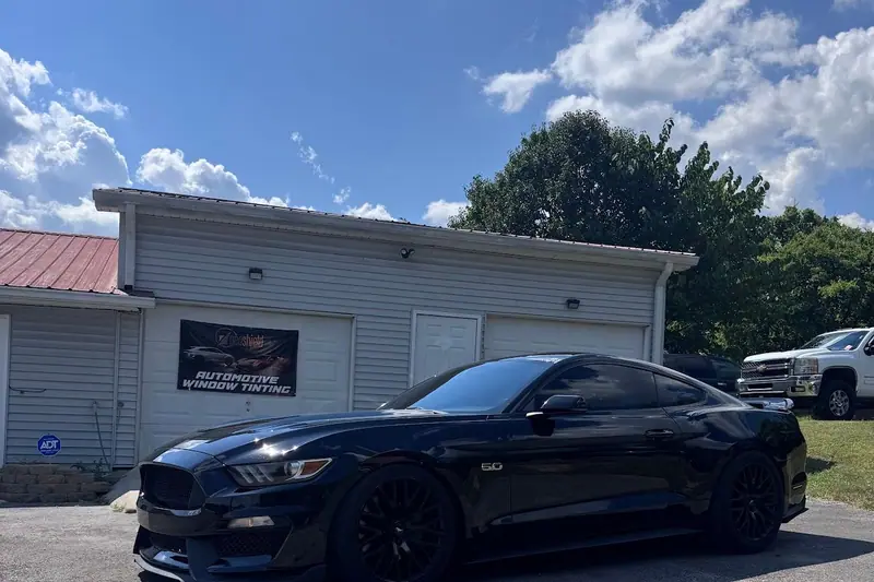 Black Ford Mustang GT parked in front of the Stealth Tint and PPF building, an Automotive Window Tinting banner on the garage door