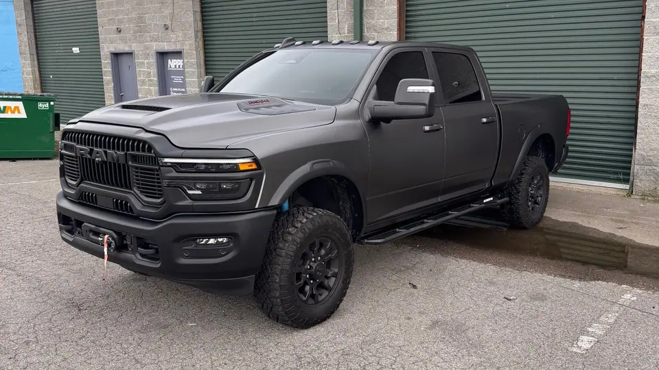 Dark gray RAM 2500 pickup with tinted windows parked by green roll-up doors