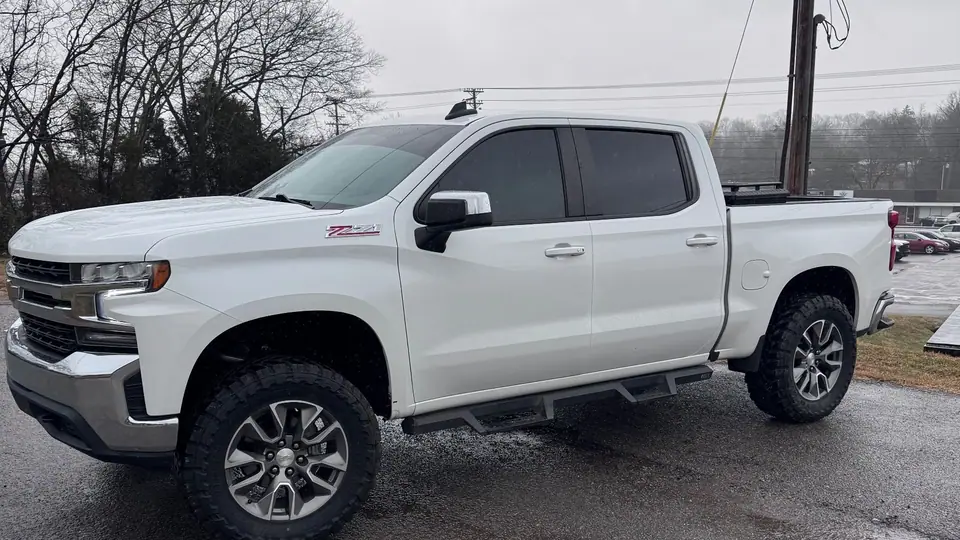 White Chevrolet Silverado with tinted windows on a lot under winter trees
