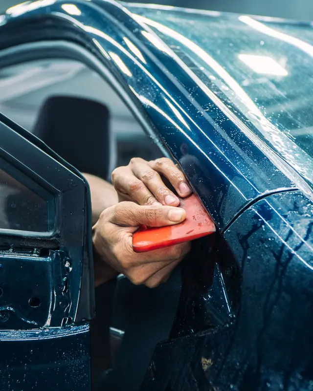 Gloved hand pressing clear protection film onto a door edge with a red squeegee (stock photo)