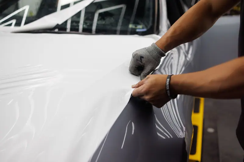 Gloved hands pulling white wrap film tight over a hood edge (stock photo)